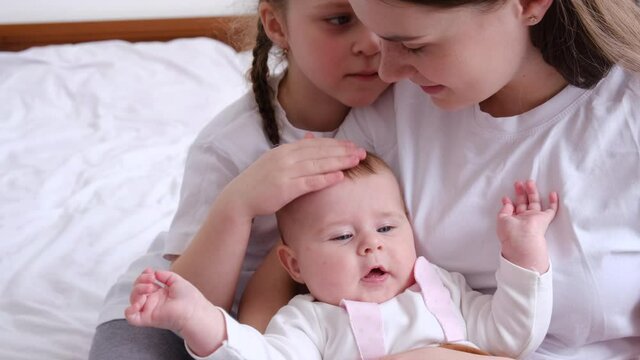 Close up of loving young mom hug cuddle little infant toddler and kiss little daughter, happy caring caucasian mother embrace lull two small girl sister child, enjoy tender moment, childcare concept