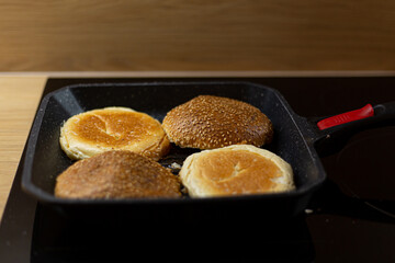 Burger bread with sesame is heating on a grill pan. Process of cooking self made burgers at home