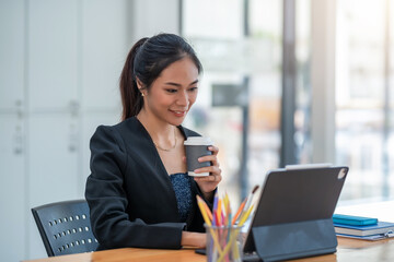Young Asian businesswoman is happy to drink coffee and working on tablet at office.