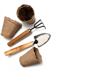 Garden tools: shovel, fertilizer, rake, peat pots with soil on a white background. Seeds and home gardening. Growing food at home. View from above. Copyspace.