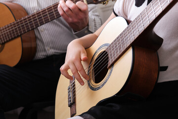 Fototapeta premium little girl and her father are playing guitar. Learning to play the guitar. Music education and extra-curricular lessons.