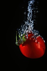 small red tomato with green leaves falling into water with air bubbles