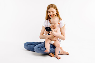 mother and her little baby are using smartphone and smiling, on white background