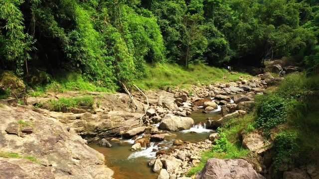 Aerial drone shot fly in enchanting forests with wild valleys with creek flowing from mountain waterfalls. The camera slowly flies forward very low. Nakhon Nayok Province, Thailand
