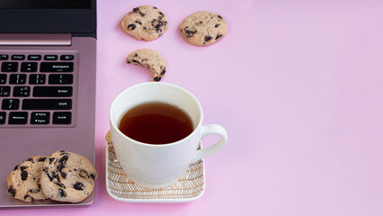 a cup of tea is on a saucer near a laptop. Cookies with chocolate on a pink background. Lifestyle concept in pink, glamorous workplace. High quality photo