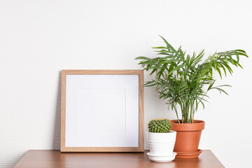 Square wooden photo frame and house plants on the table.