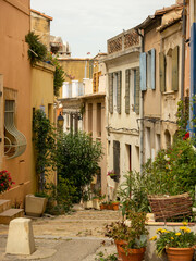 Narrow street of old city center in Arles, France, ancient houses, potted flowers, steps down.