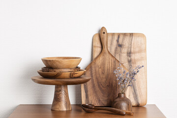 Wooden kitchenware against white wall. Boards, spoons, bowls, cake stand and vase.