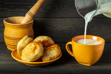 Milk is poured from a jug into an yellow mug. Idea for a delicious festive breakfast or dinner with milk and homemade donuts