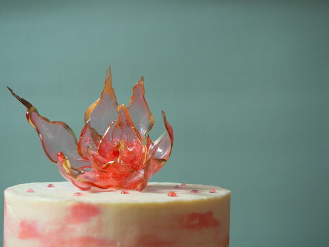 An edible red isomalt flower on top of a cake on a pale green background