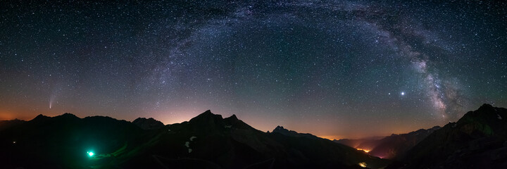 Milky Way arc and stars in night sky over the Alps. Outstanding Comet Neowise glowing at the horizon on the left. Panoramic view, astro photography, stargazing.