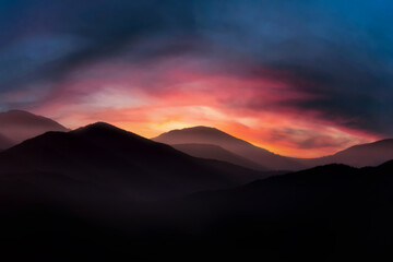 Mountain landscape at sunrise. Dramatic cloudy sunrise sky over mountain tops.