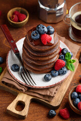 A stack of American chocolate pancakes with fresh blueberries and raspberries. Wooden background