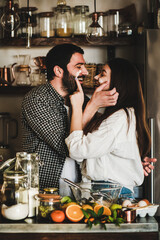 Loving young couple having fun during cooking together in kitchen. Cheerful caucasian man and brunette woman with flour on faces hugging, flirting, laughing and baking citrus cake. Valentines Day