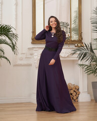 Beautiful pretty woman in long evening purple dress posing in luxury white interior. Elegant lady...