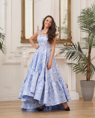 Beautiful pretty woman in long evening blue dress posing in luxury white interior. Elegant lady...