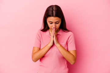 Young Indian woman isolated on pink background praying, showing devotion, religious person looking...