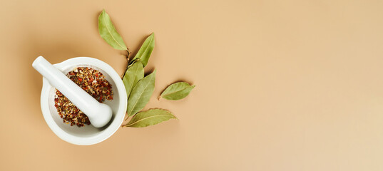 Food background with various types of spices Bay leaf, red chili pepper on a mortar with pestle on mocca beige color background with copy space. Long food banner.