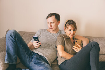 Man and woman sitting on a couch and holding smartphones in their hands.