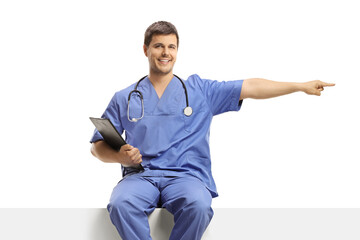 Male doctor in a blue uniform sitting on a white panel and pointing to the side