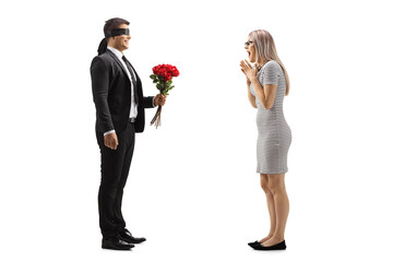 Man in a suit with blindfold giving a bunch of red roses to an excited young woman