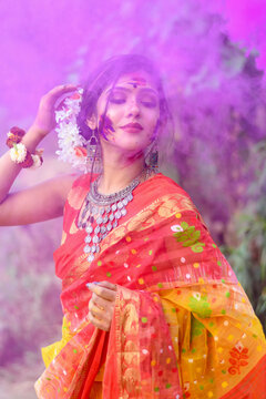 Portrait of pretty young indian girl wearing traditional saree and jewellery, playing with colors on the festival of colours called Holi, popular hindu festival celebrated across India.