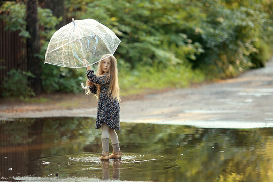 girl with long hair and wearing a dress standing in a puddle with umbrella