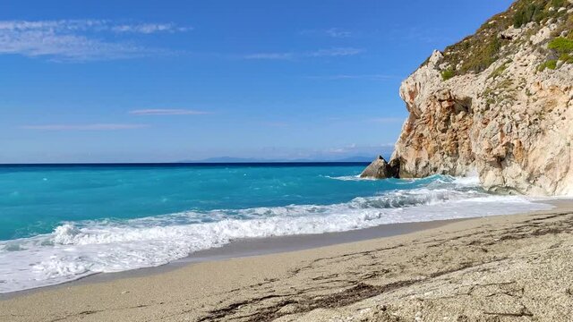 Azure bright vibrant stormy waves hitting rocky cliff on beach coast of Lefkada island in Greece. Summer wild nature travel to Ionian Sea