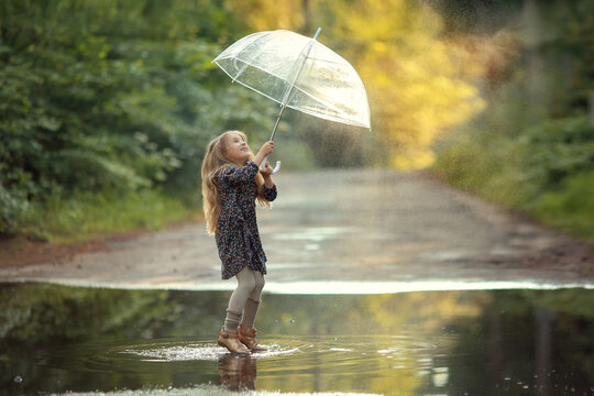 girl with long hair and with an umbrella in a dress jumping in puddles