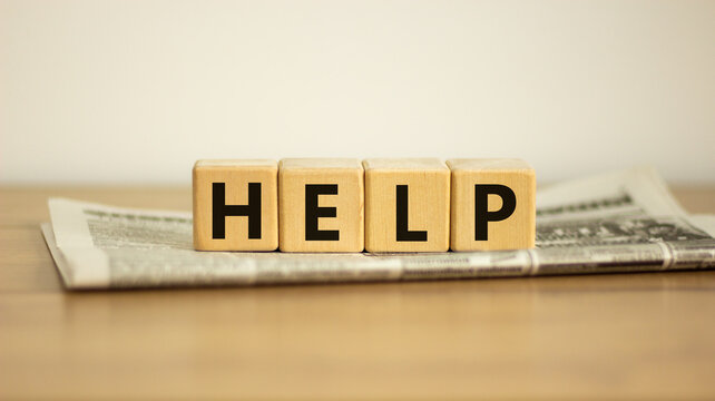 Support and help symbol. Wooden cubes with the word 'help'. Newspaper. Business, psychology, support and help concept. Beautiful wooden table, white background, copy space.