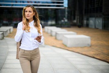 Young female manager walking outdoor while using her smartphone