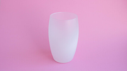 A white frosted drink glass stands on a pink background