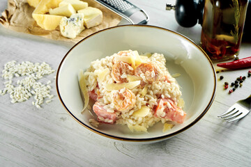 Classic Italian risotto with parmesan cheese, creamy sauce, shrimps, served in a white bowl on a wooden background. Restaurant food