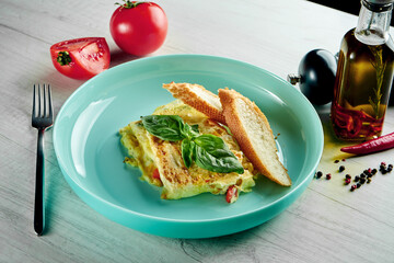 Classic French omelette with vegetables and a baguette, served in a blue plate on a wooden background. Restaurant food. scrambled eggs