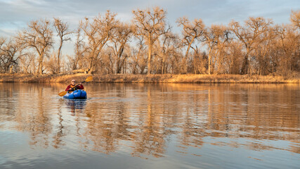 senior male is paddling an inflatable packraft on a calm lake with heron rookery in early spring in northern Colorado