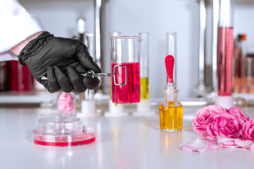 A hand in a glove holding a clip with a test tube in up-to-date perfume laboratory. Background blurred.