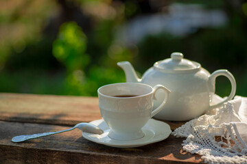 Elegant cup, lace tablecloth, teapot, wooden table. Outdoor breakfast, picnic, brunch, spring mood. Soft focus
