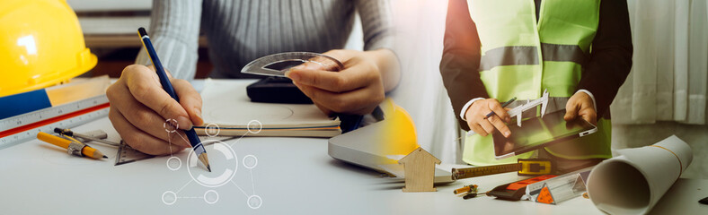 Two colleagues discussing data working and tablet, laptop with on on architectural project at construction site at desk in office