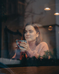 beautiful happy girl sits behind glass in a cafe. Rest by the window in the restaurant