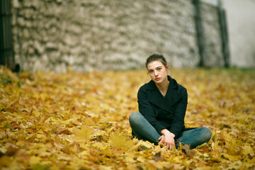 Portrait of girl sitting on fallen leaves in autumn Park.