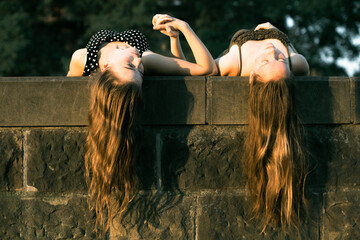 Two young girls lying on a stone slab with long hair hanging down. Beautiful soft light at sunset..