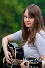Pretty teenager girl playing guitar while sitting on the stone bridge