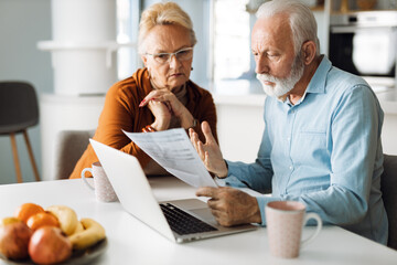 Frustrated senior couple sitting at home and checking their home finances