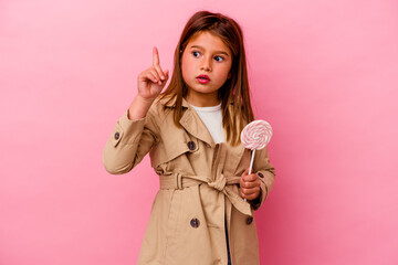 Little caucasian girl holding a lollipop isolated on pink background having some great idea, concept of creativity.