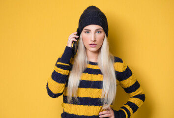 Annoyed beautiful girl on the phone, model wearing woolen cap and sweater, isolated on yellow background. Annoying woman talking on smartphone. Nuisance and smartphone