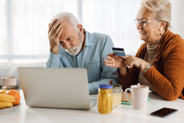 Mature woman is holding credit card while her husband is displeased