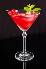 Cold cocktail with red currants in the martini glass on the black background. Location vertical.