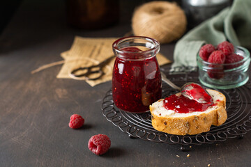 Raspberry jam in glass jar and sandwich with fresh raspberry berries on the old retro background. Selective focus.
