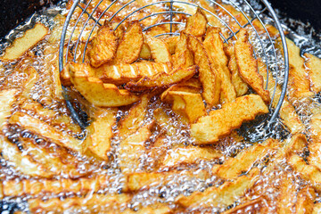 French fries are fried in a deep fat fryer. Checking the dish for readiness. Fast food. French...
