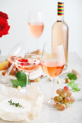 Rose wine in different wineglasses bottle on white table with grapes cheese, snacks bouquet of flowers. modern still life Rose Wine composition on light grey concrete background. Vertical photo